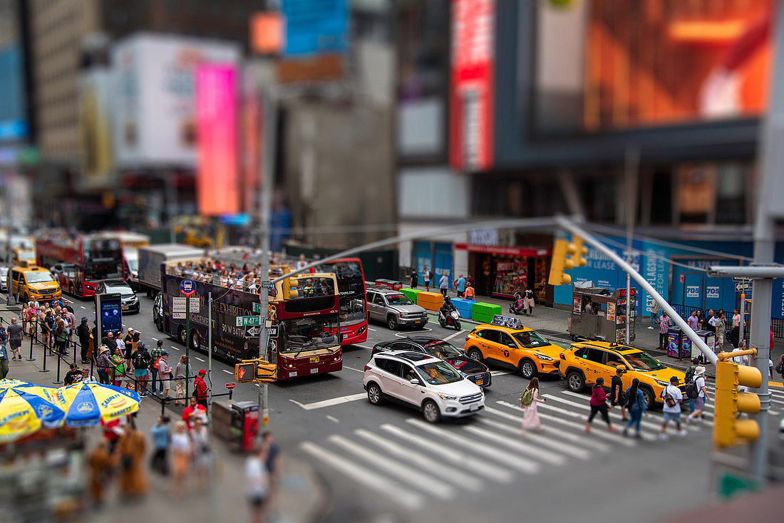 Tilt-shift photo of Times Square at W 47th Street, with a sharp band across the crosswalk and taxis, and strong blur above and below, making the scene look like a miniature diorama